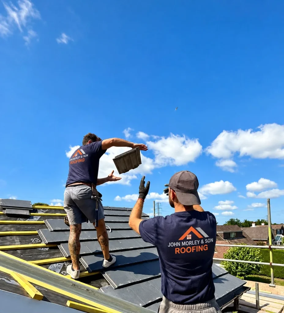 Two John Morley & Son roofers passing a tile across a new slate roof